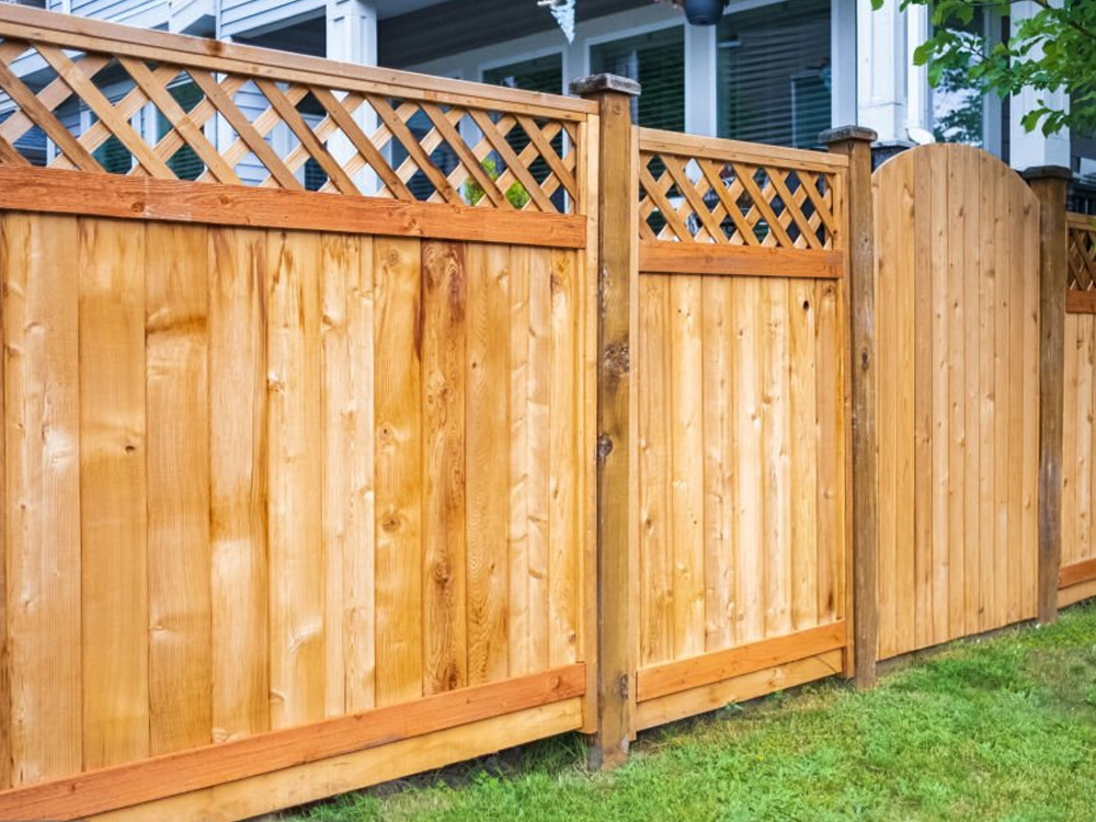 Tall wooden privacy fence with lattice-top panels along a grassy yard, including a set of gate sections and posts.