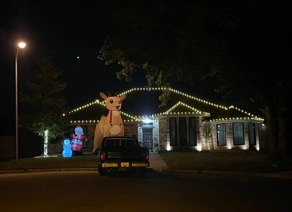 Warm white Christmas lights outlining a roofline at night with lit yard decorations