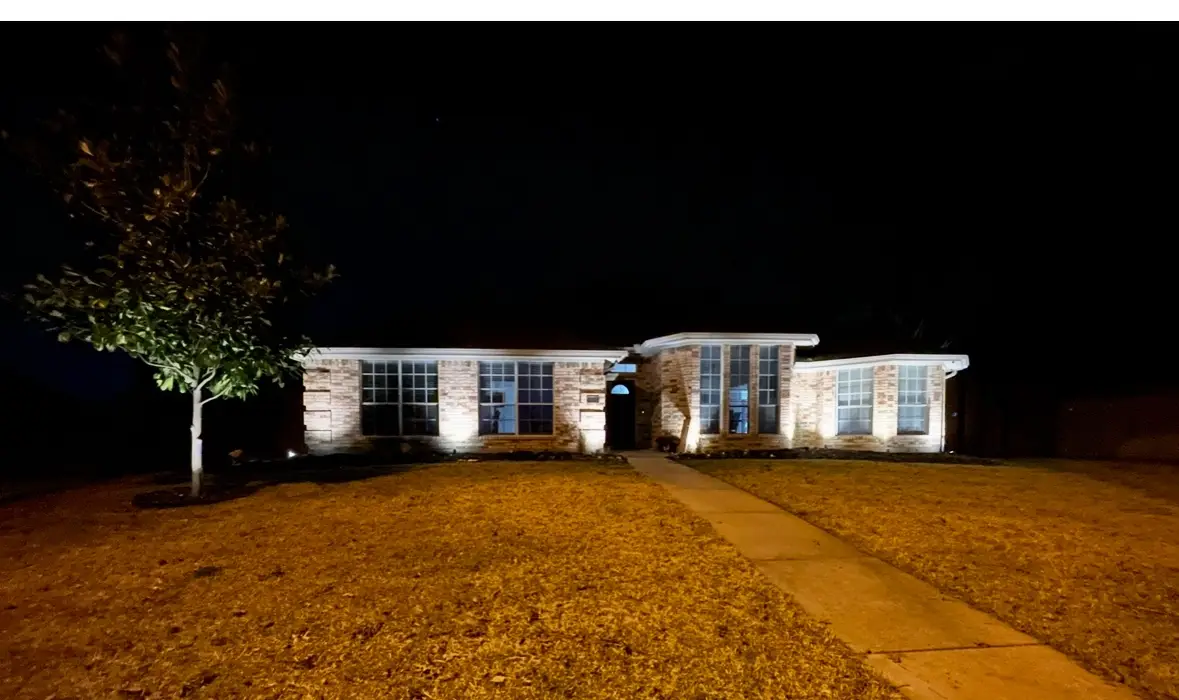 Warm uplighting washing the brick facade and front tree of a Grand Prairie home at night