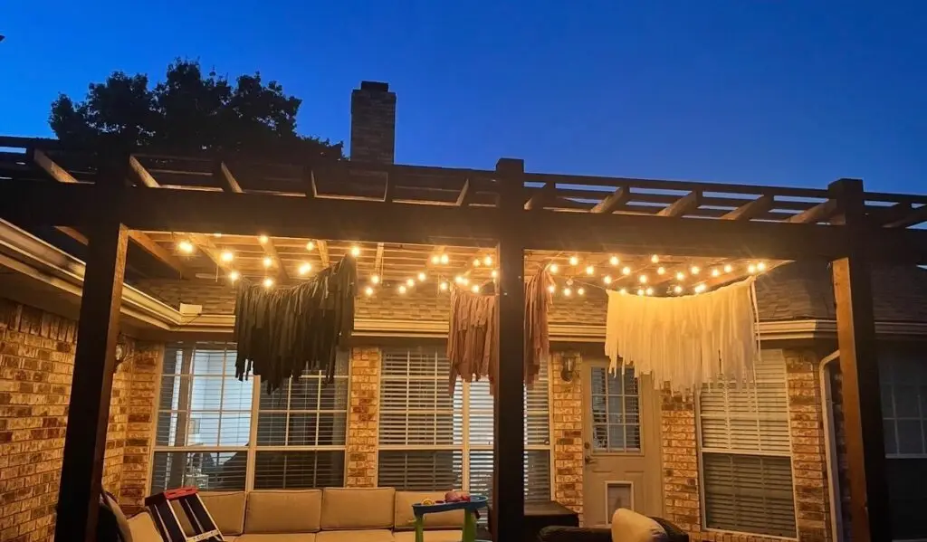 Warm string lights strung under a backyard pergola at dusk over a patio seating area