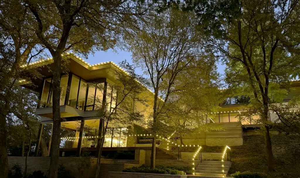 Warm roofline lights and lit stair railings on a modern hillside home at dusk